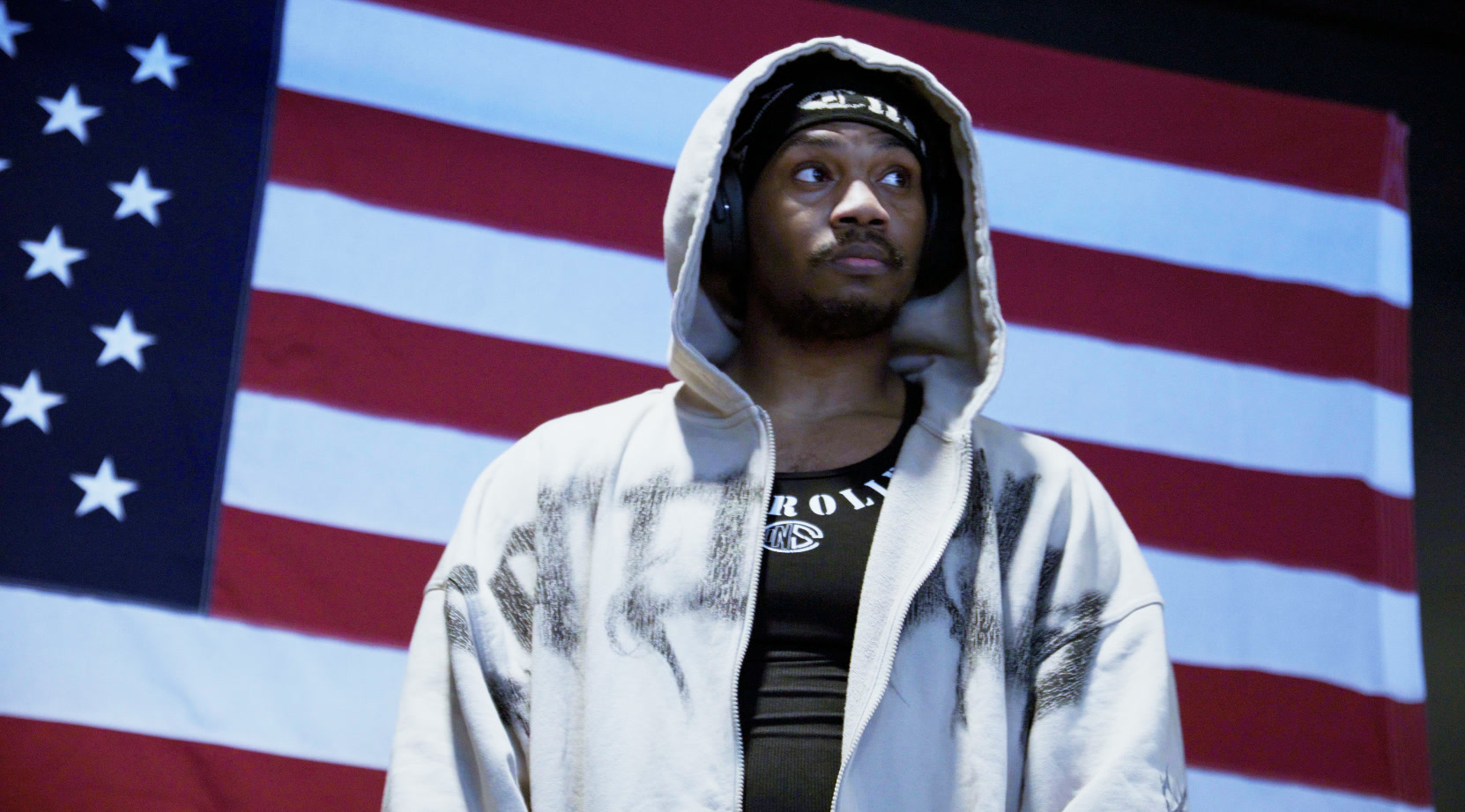 Jordan Downton in a hooded sweatshirt in front of an American flag